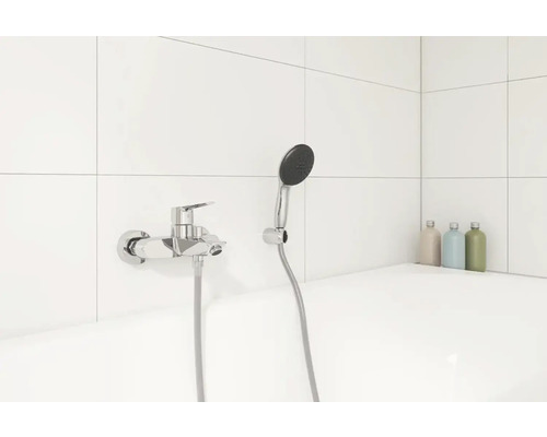 Baterie de duș aparentă cu duș de mână într-o baie cu gresie albă.