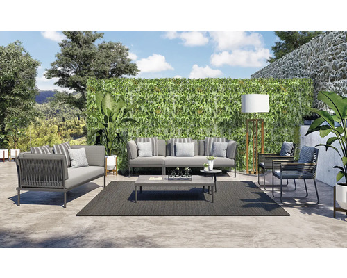 Imitație gard viu/ paravan cu frunze Fire Sky 100x200 cm verde Un set de lounge cu canapea, fotoliu, măsuță de cafea și covor afară în fața unui perete verde.
