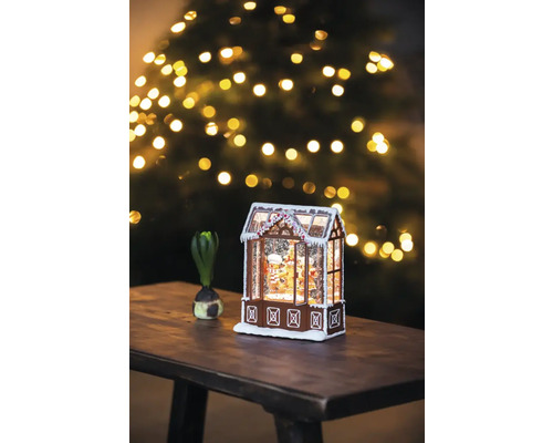 Căsuță decorativă din turtă dulce cu zăpadă și brad de Crăciun în fundal