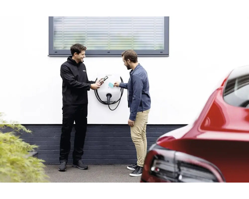 Electrician instalează o stație de încărcare pentru o mașină electrică pe peretele unei case.