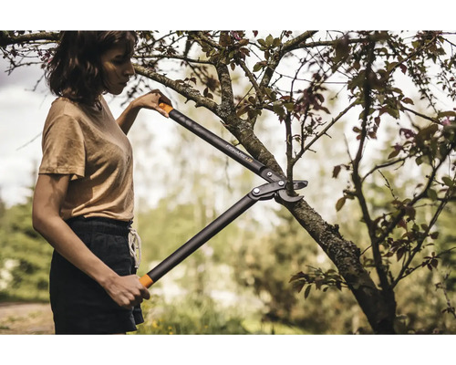 O femeie taie o ramură cu un clește de grădinărit marca Fiskars.