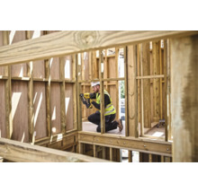 Un muncitor în construcții fixează șipci de lemn cu un capsator pneumatic în structura brută a unei case.