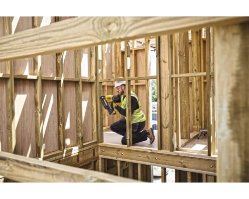 Un muncitor în construcții fixează șipci de lemn cu un capsator pneumatic în structura brută a unei case.