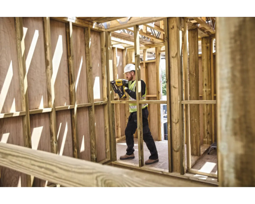 Un muncitor în construcții folosește un aparat de bătut cuie în structura brută a unei case din lemn.