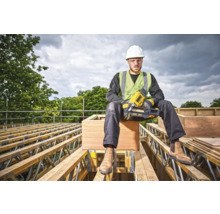 Un muncitor în construcții cu un pistol de bătut cuie DeWalt stă așezat pe o fermă de acoperiș.