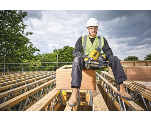 Un muncitor în construcții cu un pistol de bătut cuie DeWalt stă așezat pe o fermă de acoperiș.