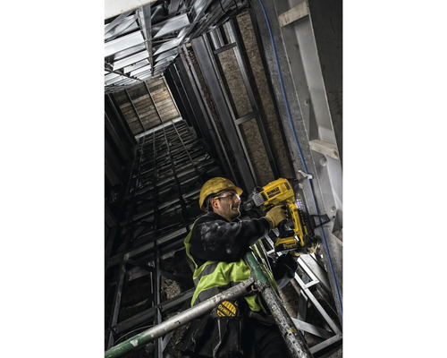 Un muncitor în construcții fixează material izolator pe un perete cu ajutorul unui pistol de bătut cuie cu acumulator DeWalt.