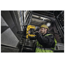 Un muncitor în construcții folosește un aparat de bătut cuie fără fir DeWalt pe un șantier.