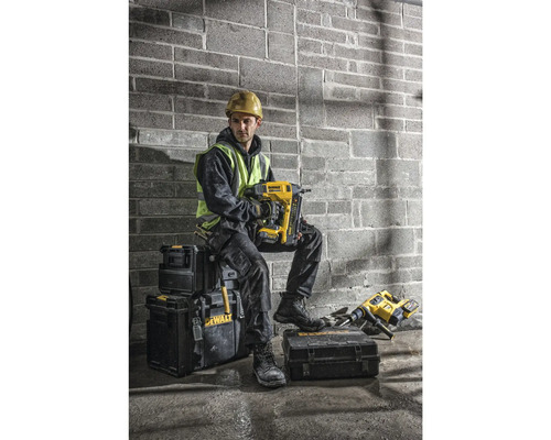Un meșter cu cască de protecție și vestă reflectorizantă stă așezat pe cutii de scule și ține un pistol de bătut cuie galben marca DeWalt.