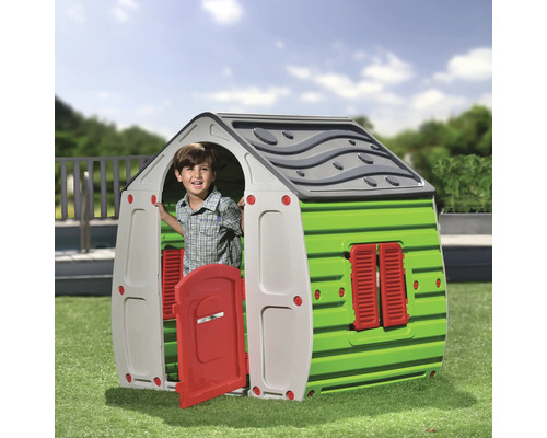 Copil într-o căsuță de joacă verde și gri cu o ușă roșie pe gazon