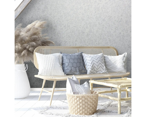 Scenă decorativă cu bancă de ratan, perne, masă de ratan și vază de flori în fața unui tapet floral