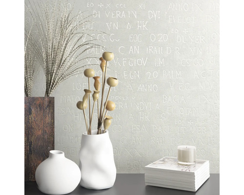Interior decorativ cu vaze, flori uscate, carte și lumânare în fața unui perete cu model de litere