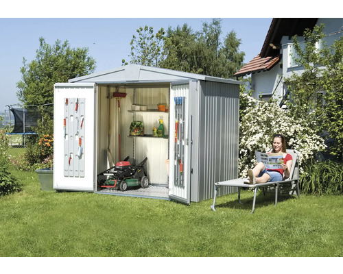 Scenă de grădină cu magazie de scule, mașină de tuns iarba și femeie relaxându-se pe un șezlong