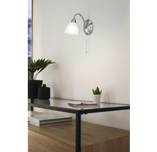 Lumină de perete metalică cu abajur din sticlă deasupra unui raft cu plante și decor