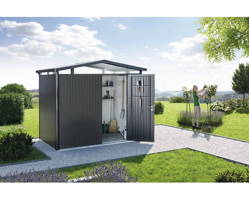 Șopron de grădină cu ușa deschisă într-un peisaj de grădină cu gazon și o femeie care taie trandafiri.