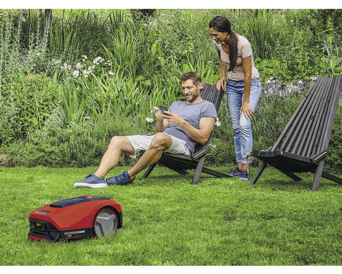 Scenă de grădină cu robot de tuns iarba, două scaune din lemn și două persoane