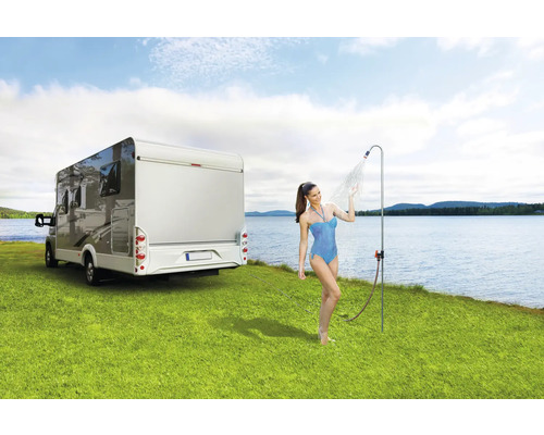 Femeie sub duș de camping lângă rulotă pe gazon lângă lac