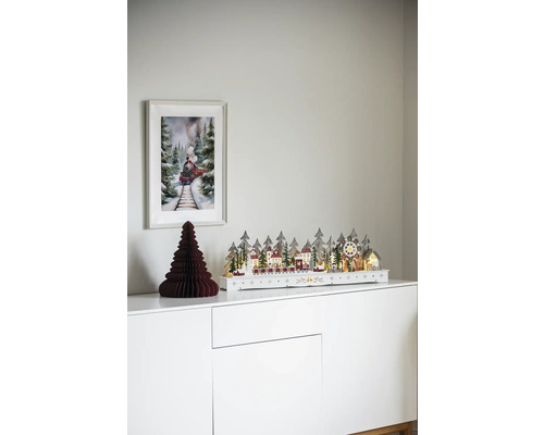 Scenă decorativă de Crăciun cu peisaj de iarnă iluminat, brad de hârtie și imagine cu tren pe un dulap alb