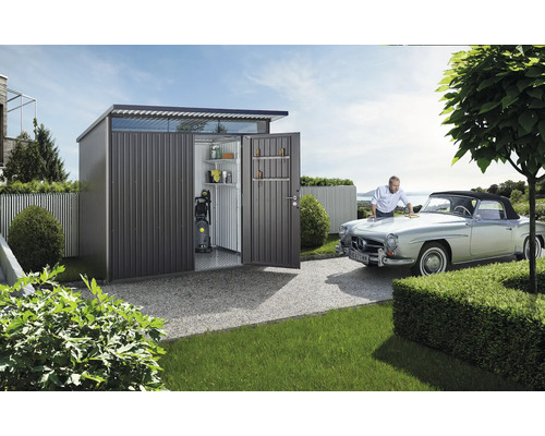 Magazie metalică cu uși deschise, rafturi, mașină de spălat cu presiune și un bărbat care lustruiește o mașină.