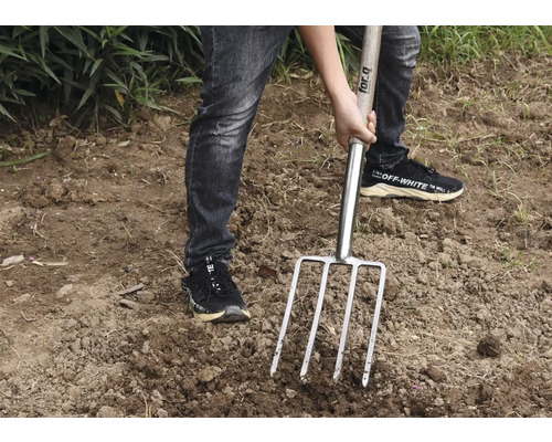 O persoană folosește o furcă de gunoi de grajd în grădină.