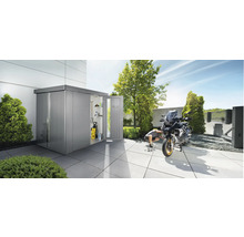 Scenă de grădină cu căsuță de grădină metalică, motocicletă și bărbat care efectuează lucrări de întreținere