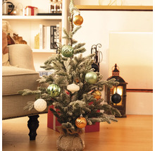 Brad mic de Crăciun decorat pe podea cu cadouri și decorațiuni în fundal.