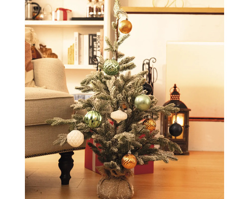 Brad mic de Crăciun decorat pe podea cu cadouri și decorațiuni în fundal.