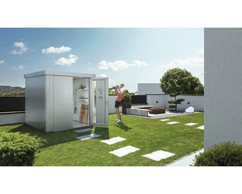 Dulap de grădină metalic cu ușa deschisă pe un gazon, o femeie ține un copil sus.