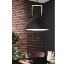 Lampa suspendată neagră cu cadru din lemn deasupra unei mese de sufragerie în fața unui perete de cărămidă.