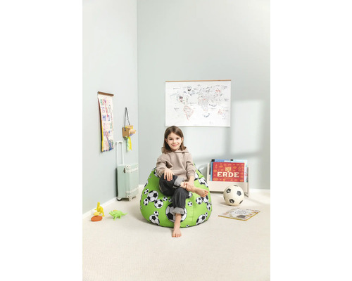 Un copil stă așezat pe un sac de fasole verde cu model de fotbal într-o cameră luminoasă.