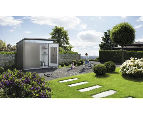 Magazie metalică de grădină cu ușa deschisă într-o grădină cu copii care se joacă.