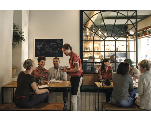 Scenă într-un restaurant cu clienți la mese și un chelner care preia comenzi.