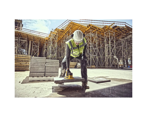 Un muncitor în construcții folosește o mașină de șlefuit pe o placă de piatră pe un șantier.