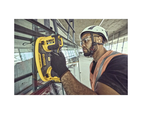 Un muncitor în construcții folosește un dispozitiv de ridicat sticlă DeWalt pe un șantier pentru a instala o fereastră.