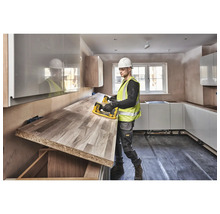 Un bărbat cu cască de protecție și vestă de siguranță transportă un blat de lucru într-o bucătărie.