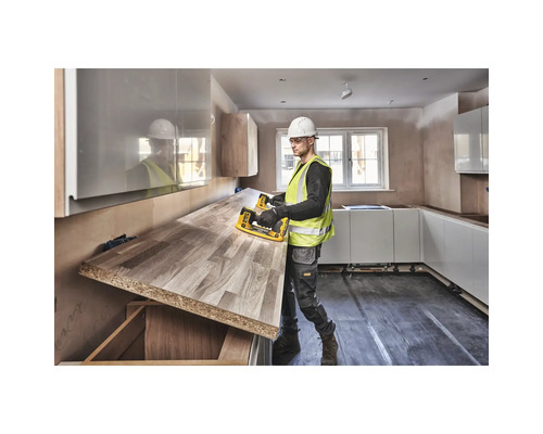 Un bărbat cu cască de protecție și vestă de siguranță transportă un blat de lucru într-o bucătărie.