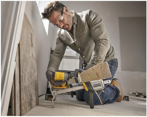 Un bărbat stă în genunchi și lucrează cu o șurubelniță cu impact fără fir și o menghină pe o scândură de lemn