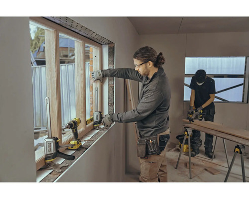 Doi meseriași montează o fereastră cu scule într-o clădire la stadiul de construcție brută.