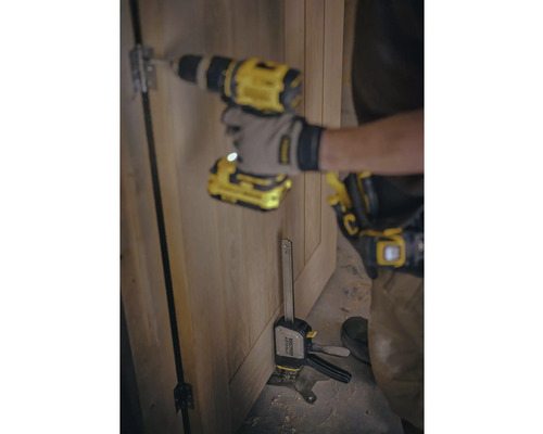 Un meseriaș montează o balama de ușă pe o ușă de lemn cu ajutorul unei mașini de găurit cu acumulator și a unei menghine cu șurub.