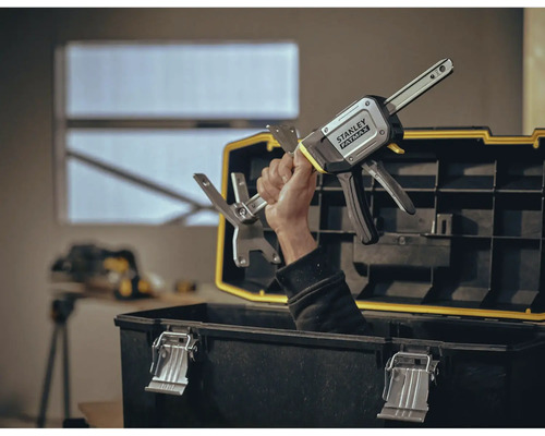 Mână ținând clemă cu o singură mână Stanley Fatmax deasupra cutiei de scule