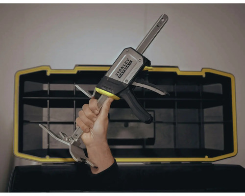 O mână ține o menghină cu o singură mână Stanley Fatmax în fața unei cutii de scule.