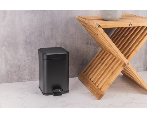 Coș de gunoi negru din metal lângă un taburet din lemn.