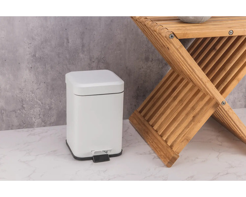 Coș de gunoi cu pedală alb din metal lângă un taburet din lemn