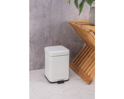 Coș de gunoi alb cu pedală, din metal, lângă o măsuță laterală din lemn