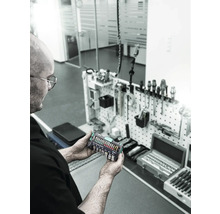 O persoană ține un set de instrumente Wera Tool-Check Plus 1 în fața unui perete cu unelte.