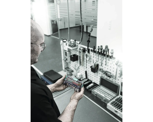 O persoană ține un set de instrumente Wera Tool-Check Plus 1 în fața unui perete cu unelte.