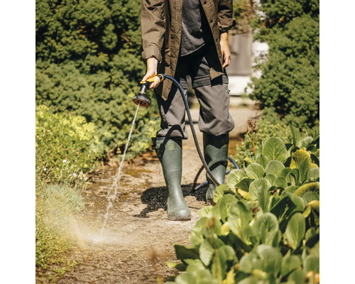 O persoană udă o potecă din grădină cu un pulverizator de grădină.