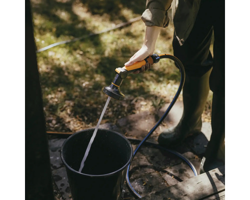 O persoană umple o găleată cu un pulverizator de grădină