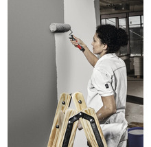 Femeie vopsind un perete cu trafaletul, stând pe o scară