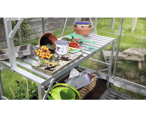 Seră cu masă de plantare, ghivece și unelte de grădinărit.